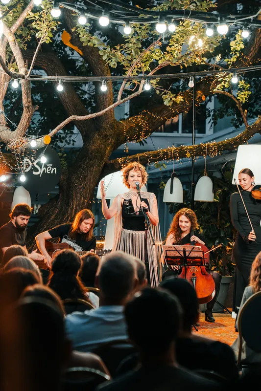 The whole band under the lit tree canopy at twilight, D'Shen centre with a raised hand
