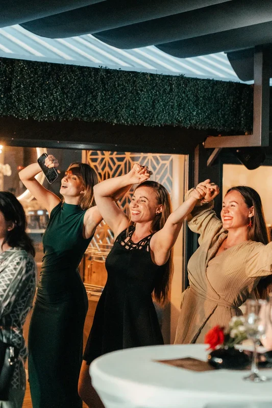Women dancing with raised arms among cocktail tables